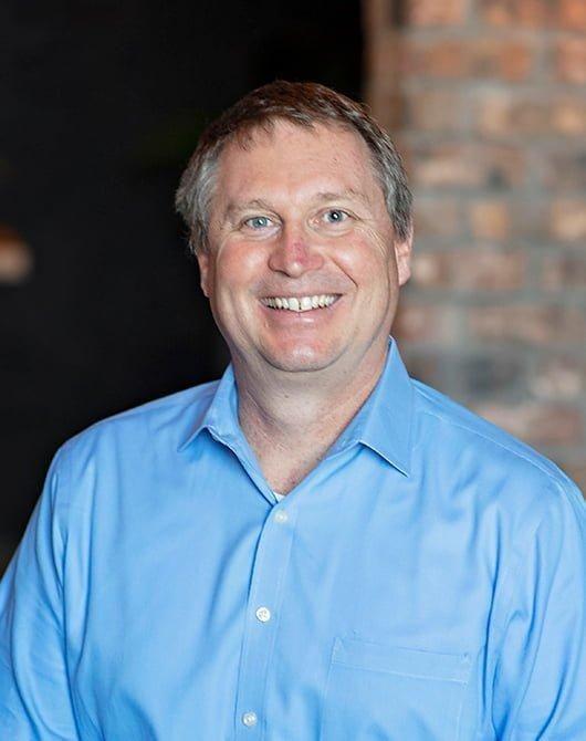 Smiling man with short brown hair in a light blue shirt.