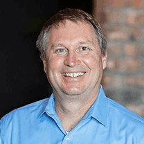 Smiling man with short brown hair in a light blue shirt.